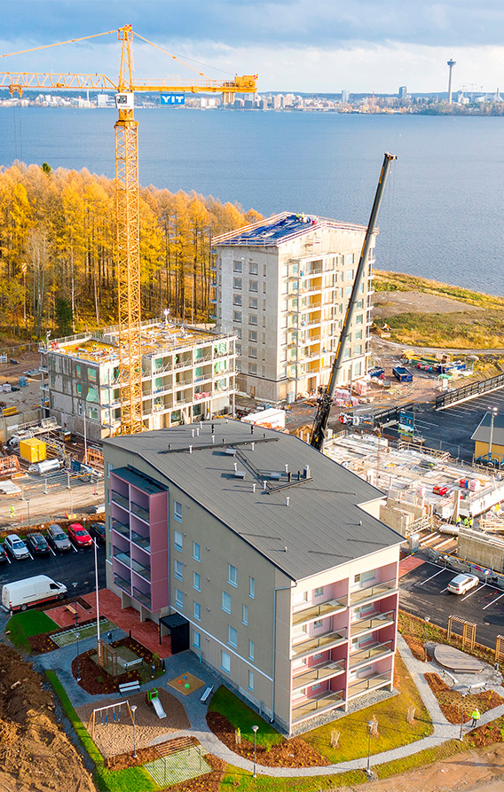 Ilmakuva, jossa näkyy Raamikadulle valmistunut kerrostalo, rakenteille olevia naapurikerrostaloja, nostokurki ja taustalla on järvi. Horisontissa näkyy Näsinneula.